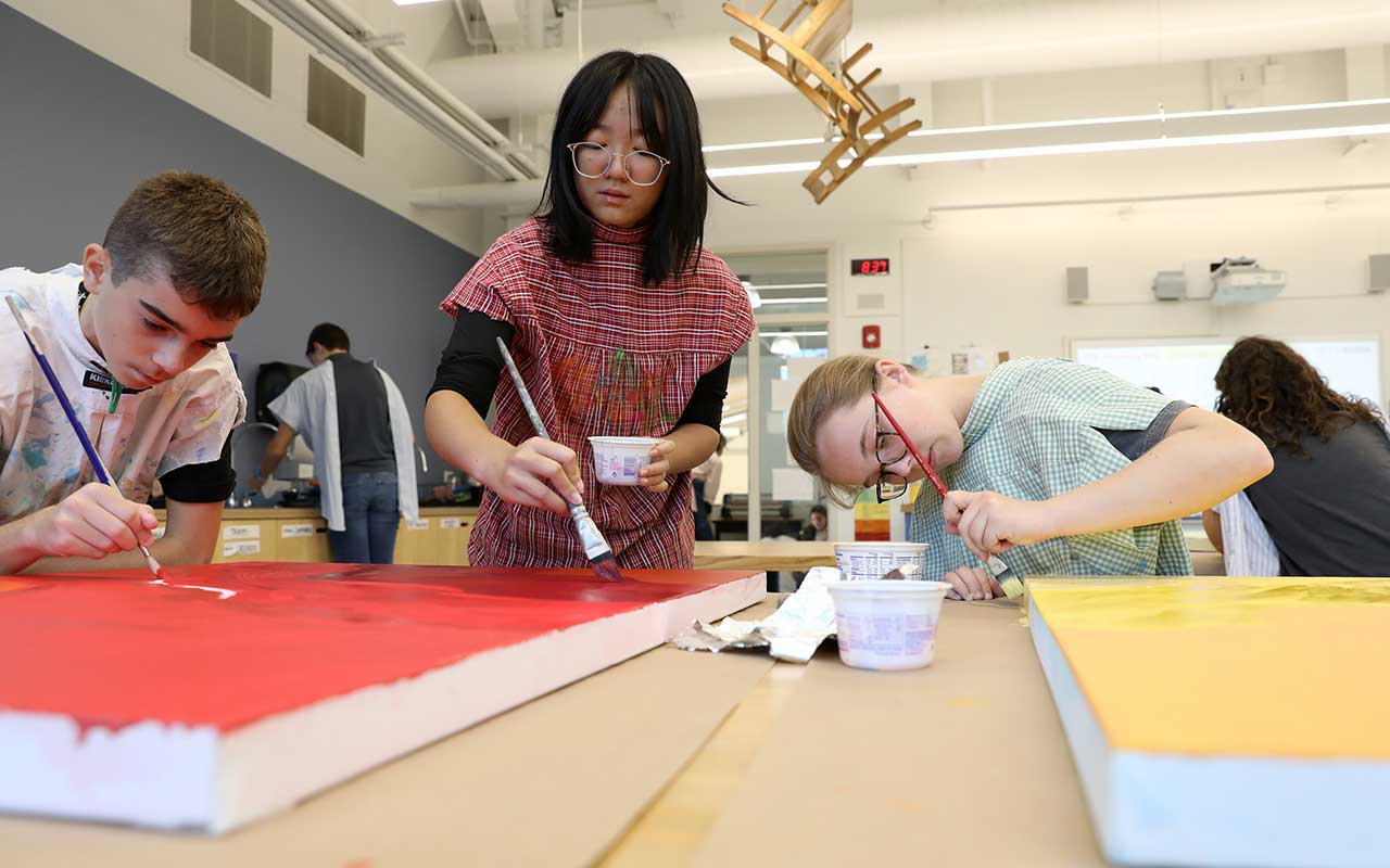 Three students work on large canvases in the mural elective