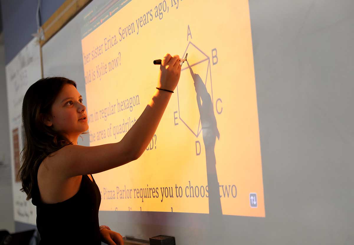 A girl solves a math problem at the white board